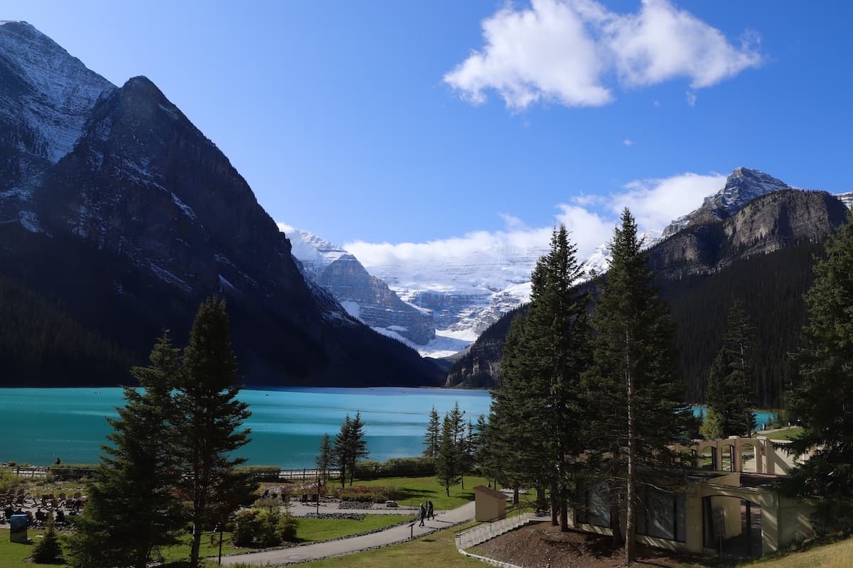 Blue lake surrounded by pine trees and blue sky with mountains in background.