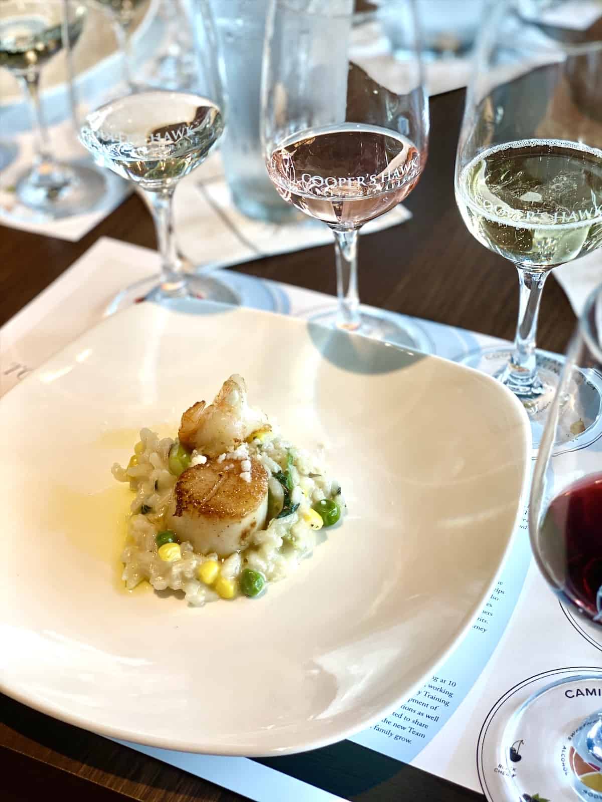 Scallops and risotto with wine glasses in background.