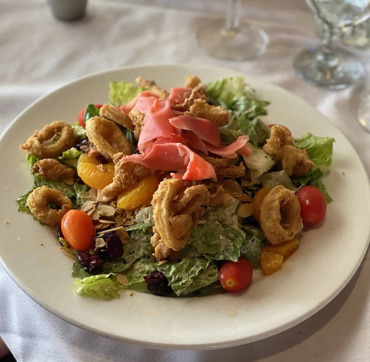 Calamari on a salad with fresh ginger in a white bowl.