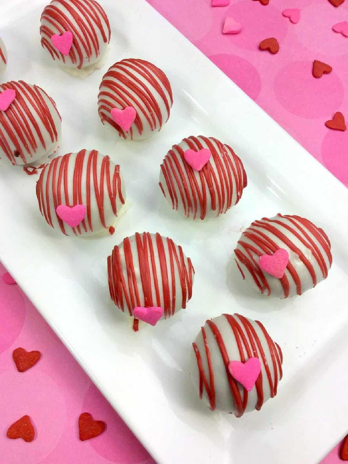 White chocolate covered cake balls with pink chocolate drizzle and candy heart sprinkles.