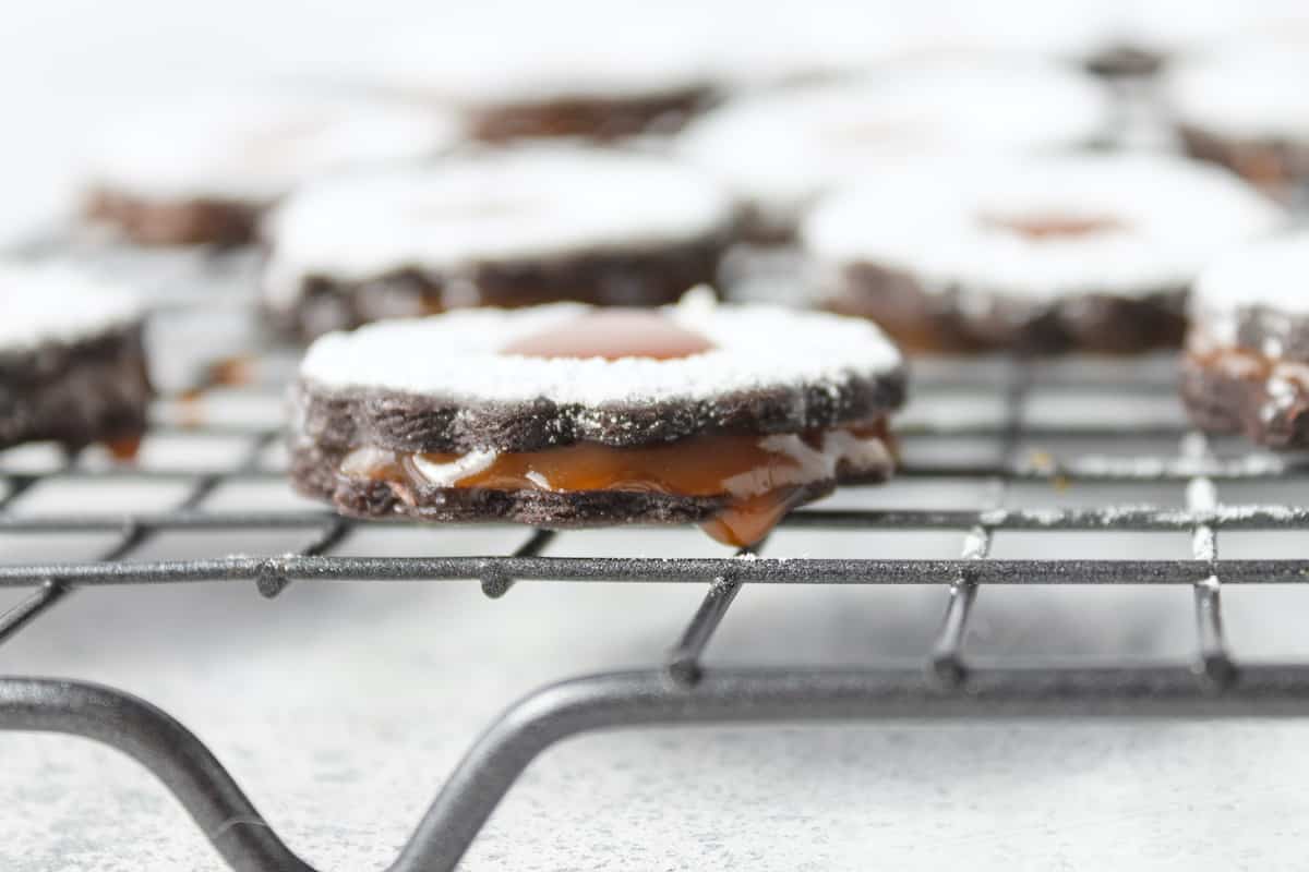 Salted caramel cookies topped with powdered sugar dripping on wire rack.