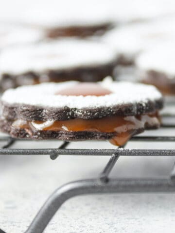 Chocolate cookie with caramel dripping out, topped with powdered sugar set on a wire rack.