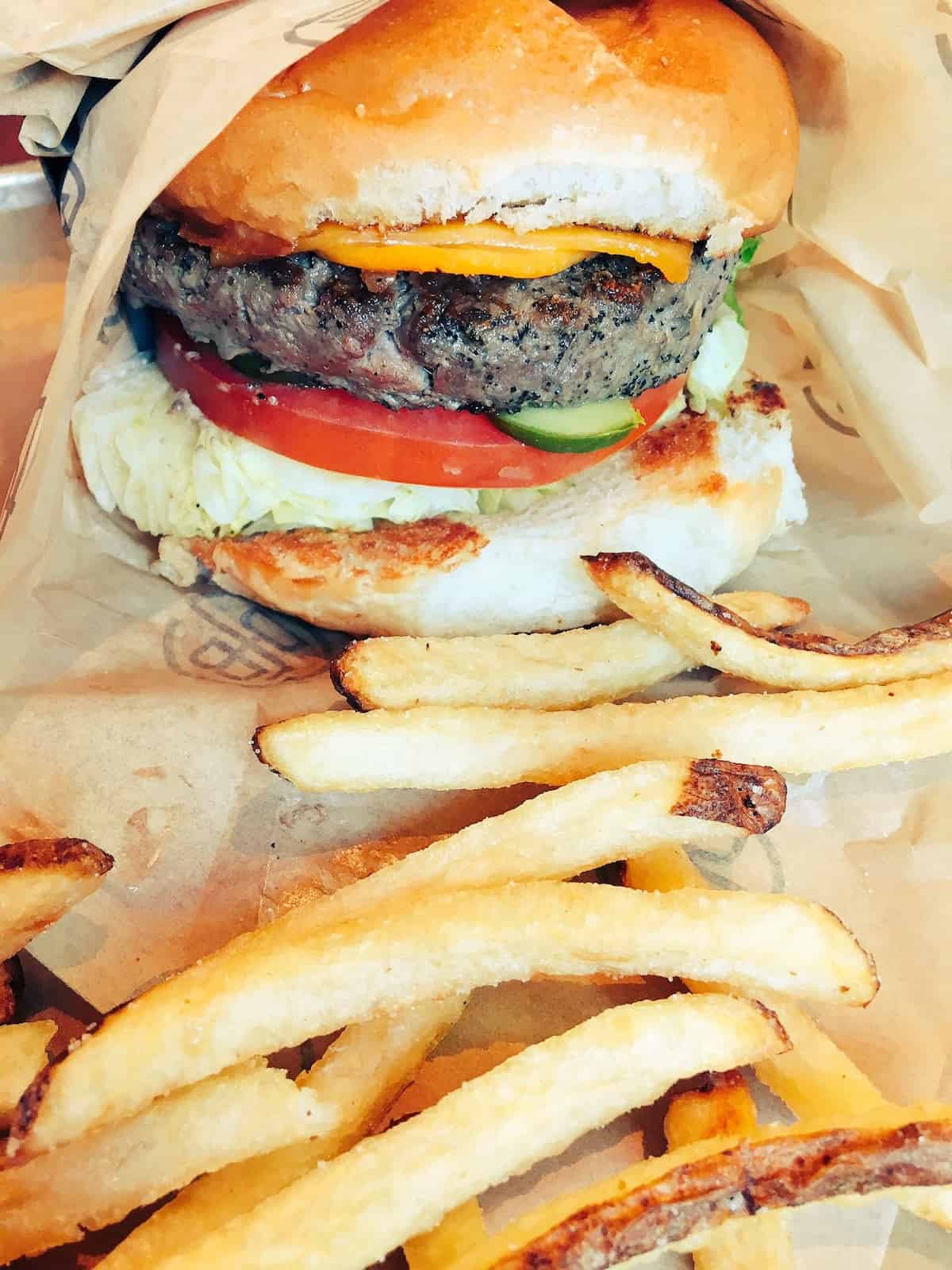 Cheeseburger with tomato, lettuce, and pickles with French fries wrapped in paper.
