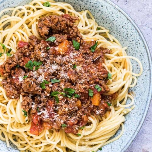 Pasta with bolognese sauce on a grey spotted plate.