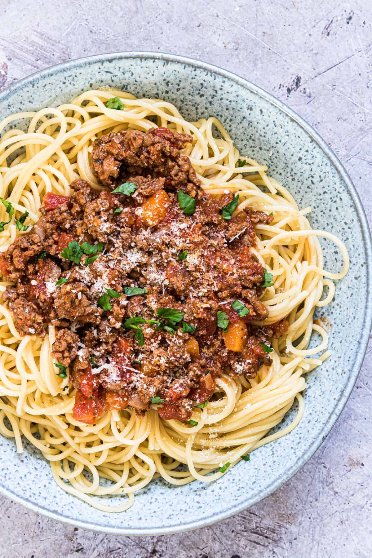 Pasta with bolognese sauce on a grey spotted plate.