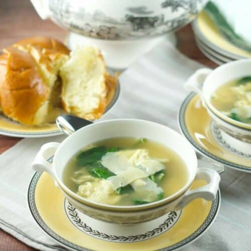 Stracciatella soup in a white bowl with bread in background.