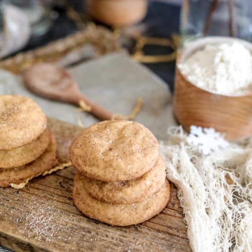 Snickerdoodle cookies on a wood board with white netting, flour and spoon in background.