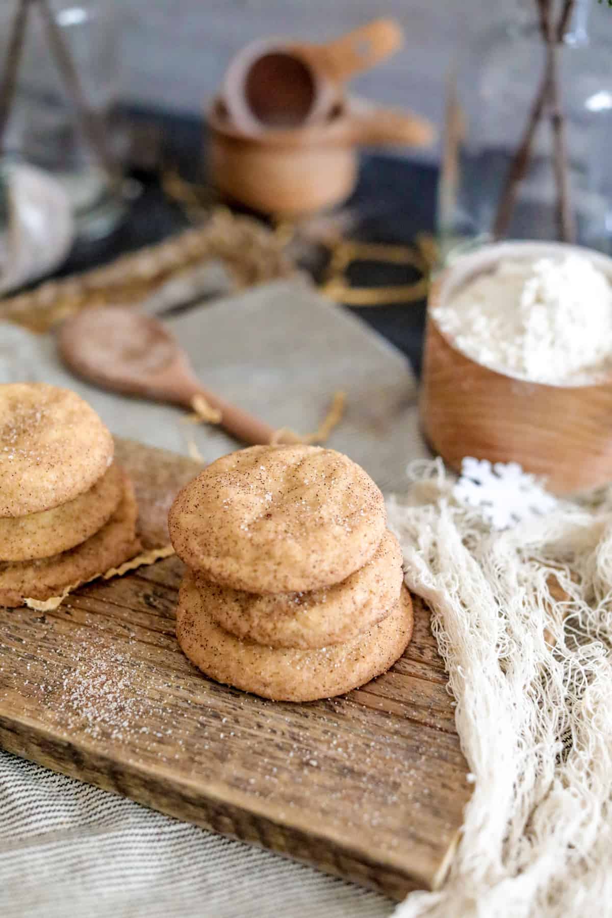 Snickerdoodle cookies on a wood board with white netting, flour, and spoon.