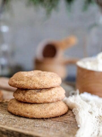 Snickerdoodle cookies on a wood board with a cream colored cloth with flour in background.