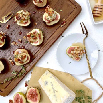 Fresh figs with blue cheese, walnuts, and honey on a cutting board with block of blue cheese.
