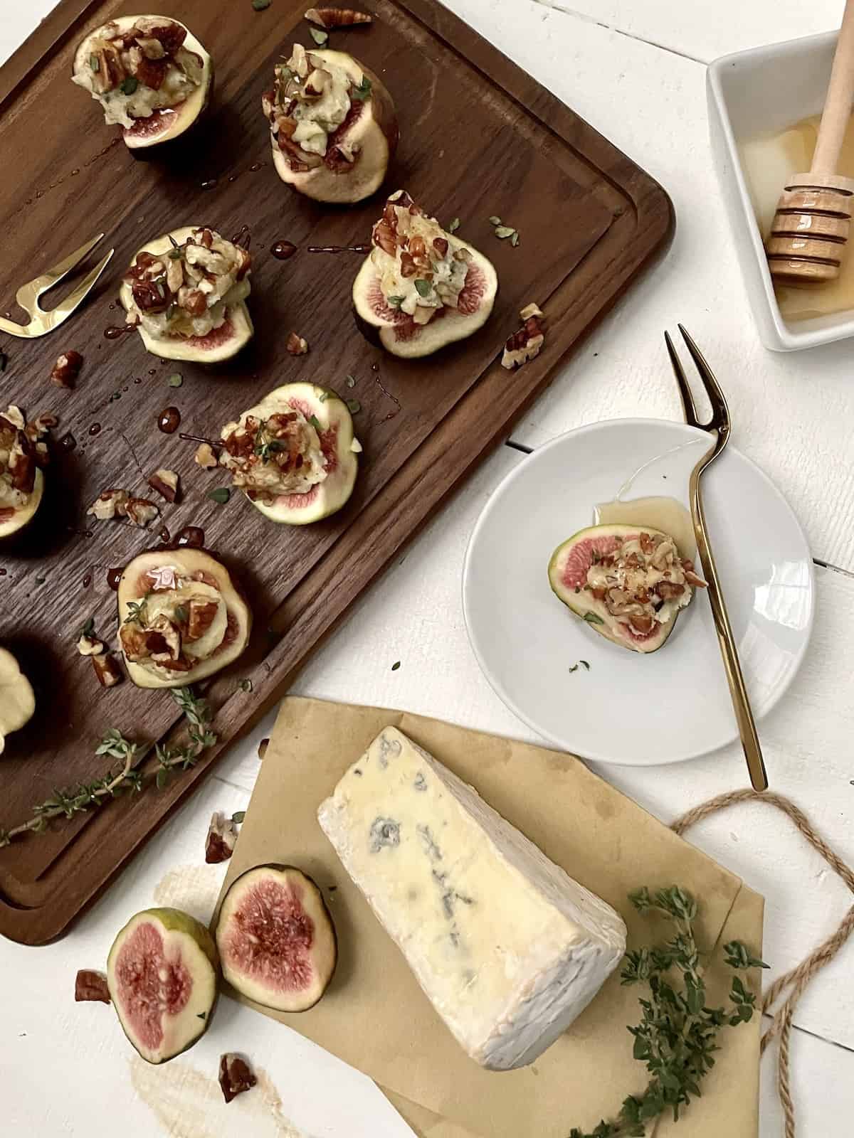 Fig with cheese, nuts, honey, and thyme on wood board with piece of cheese and thyme.