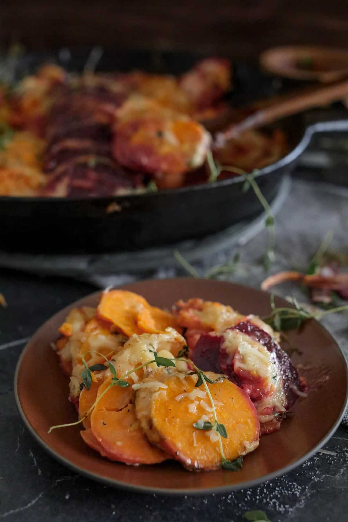 Root vegetables on a plate with root vegetable casserole in cast iron skillet in the background.