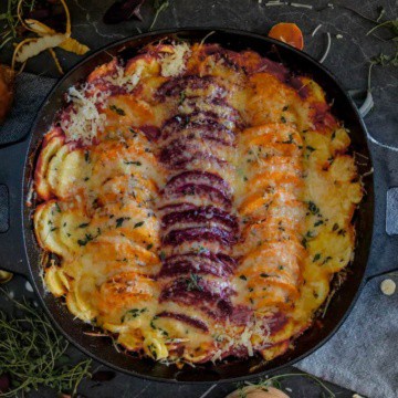 Root vegetables in a black pan with cheese on top.