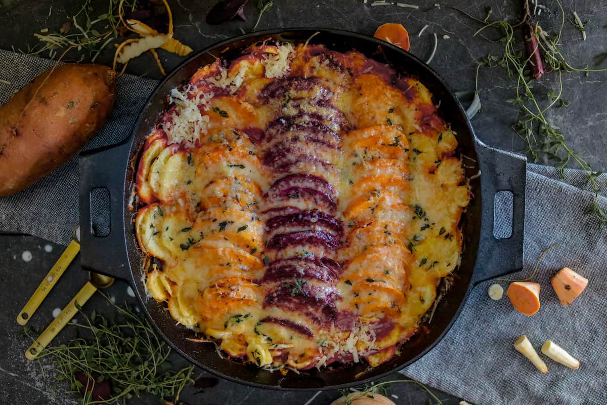 Finished root vegetable dish with cheese on top in black pan.