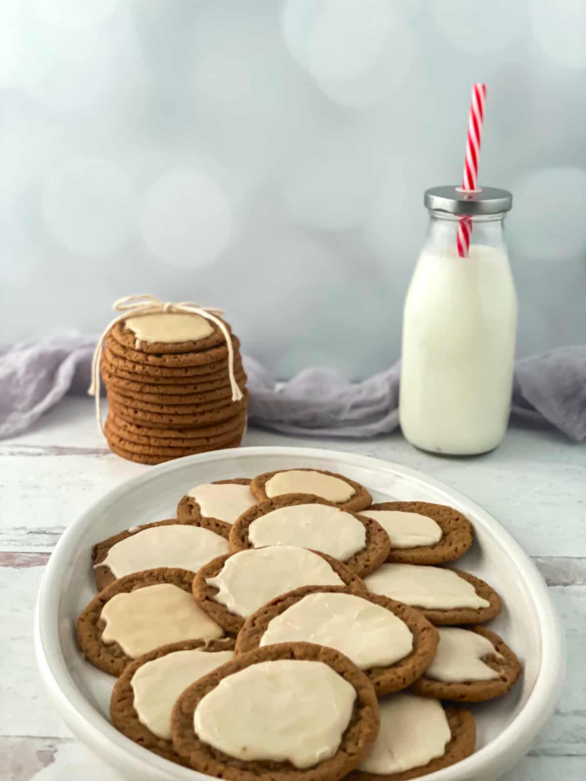 Cookies with icing on a white plate on a white counter with a bottle of milk with a straw.
