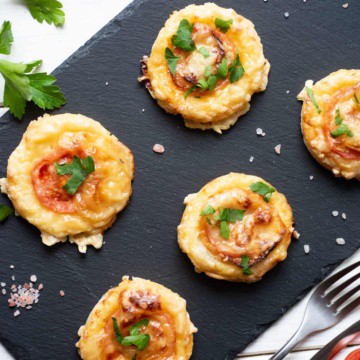Tomato tarts on a black board with salt, pepper, parsley, and tomato.