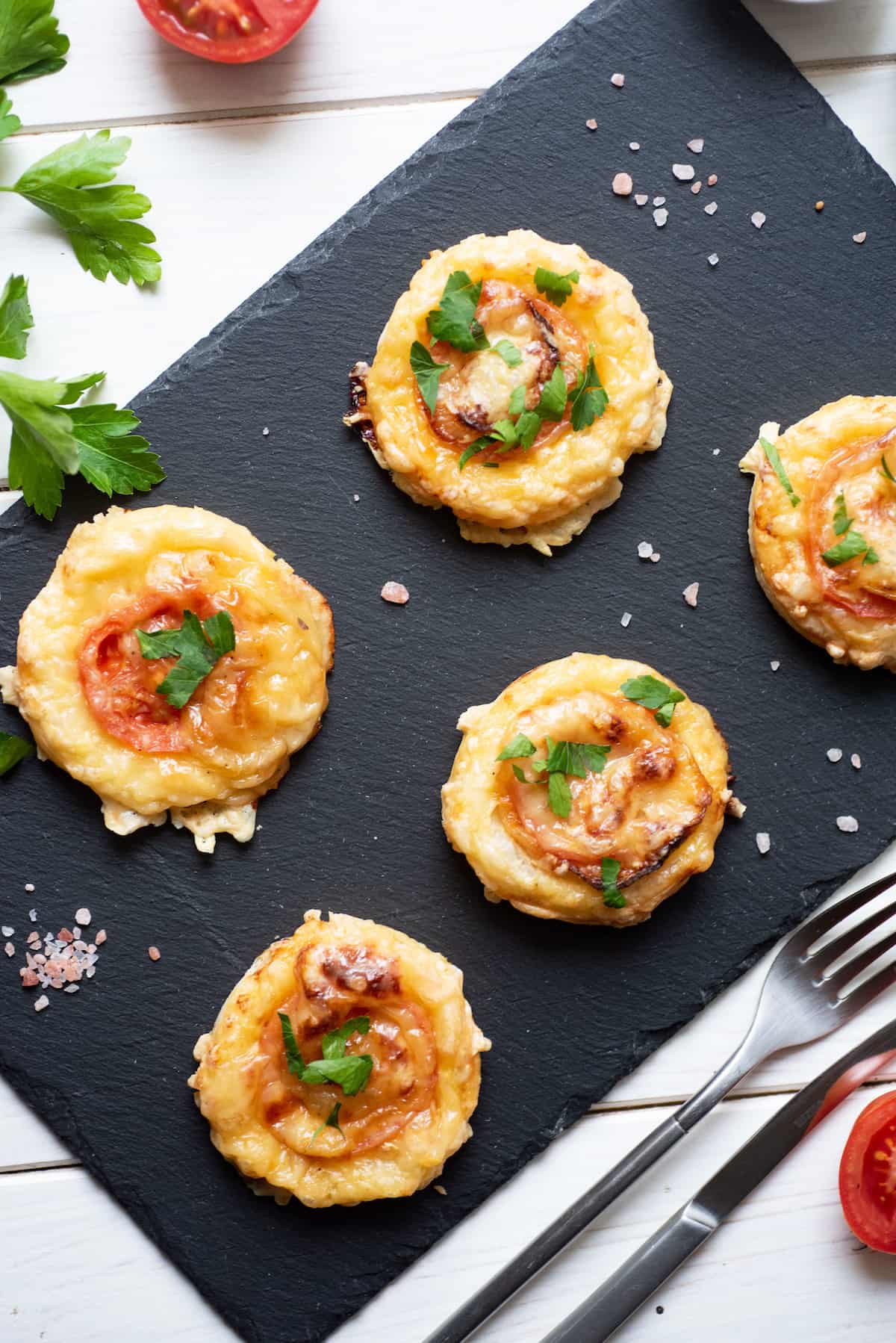 Tomato tarts on a black board with salt, pepper, parsley, and tomato.