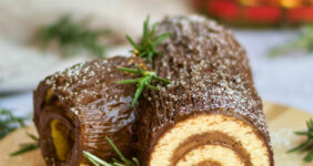 Chocolate rolled cake on a wood board with Christmas decor for Pinterest.