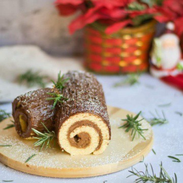Chocolate rolled cake on a cutting board with greenery and Christmas decor in background.