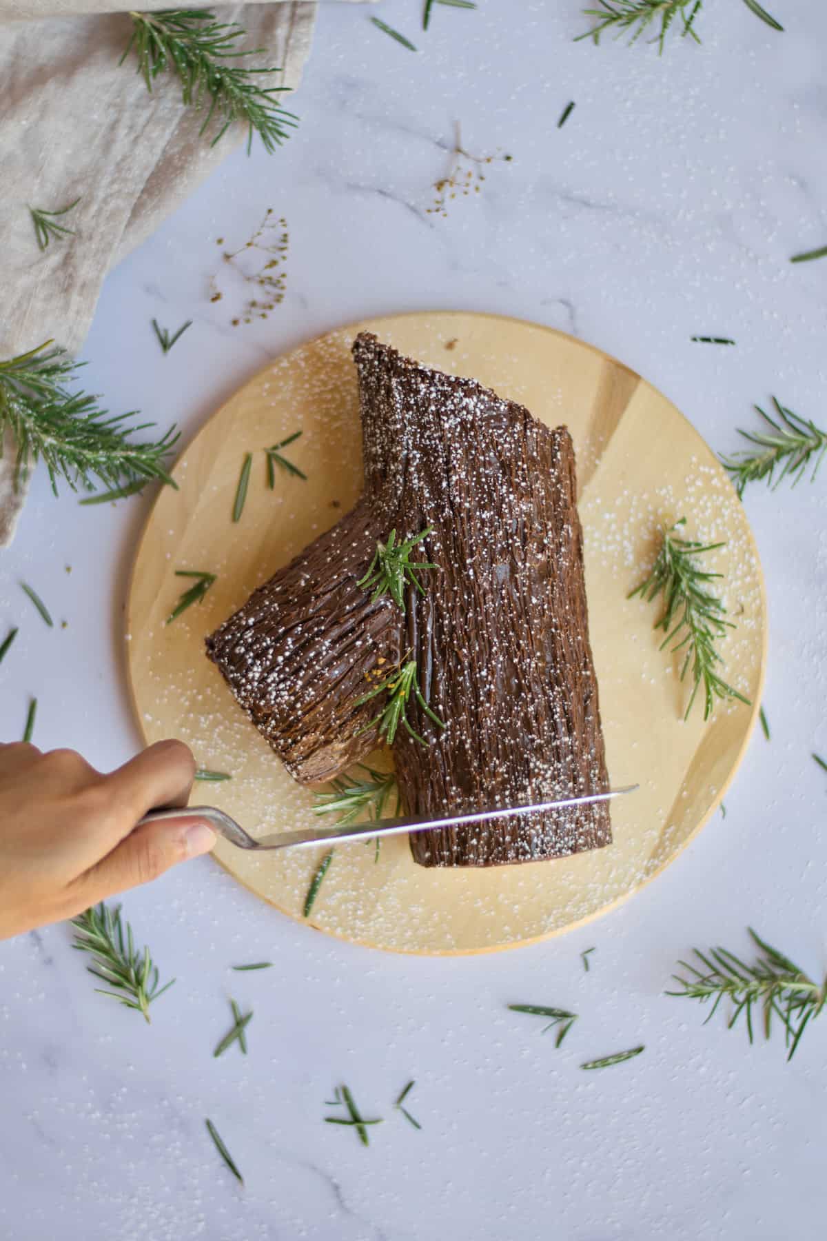 Chocolate rolled cake to look like yule log from above with knife cutting.
