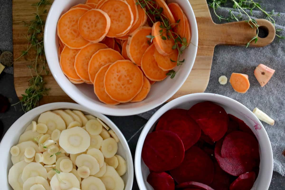 Sliced sweet potatoes, beets, and parsnips in bowls.