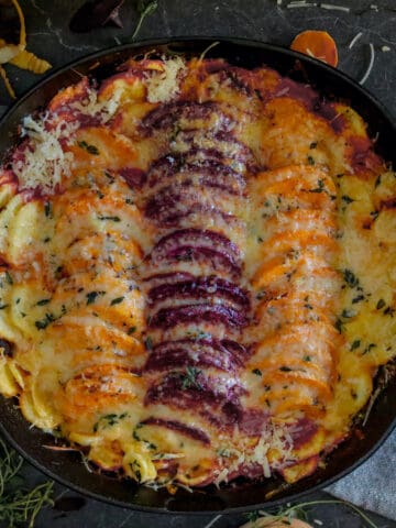 Baked root vegetables with cheese in a cast iron skillet.