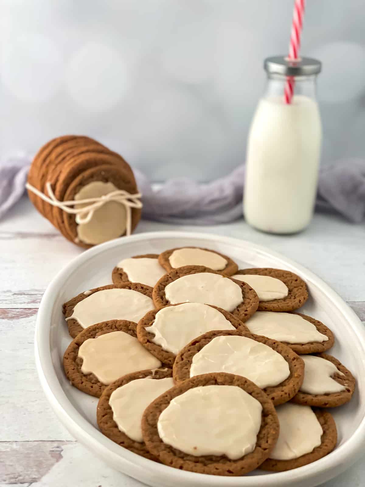 Cookies with icing on a white plate on a white counter with a bottle of milk with a straw.