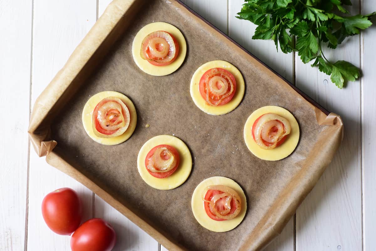 Pastry rounds with tomato and onion on baking sheet.