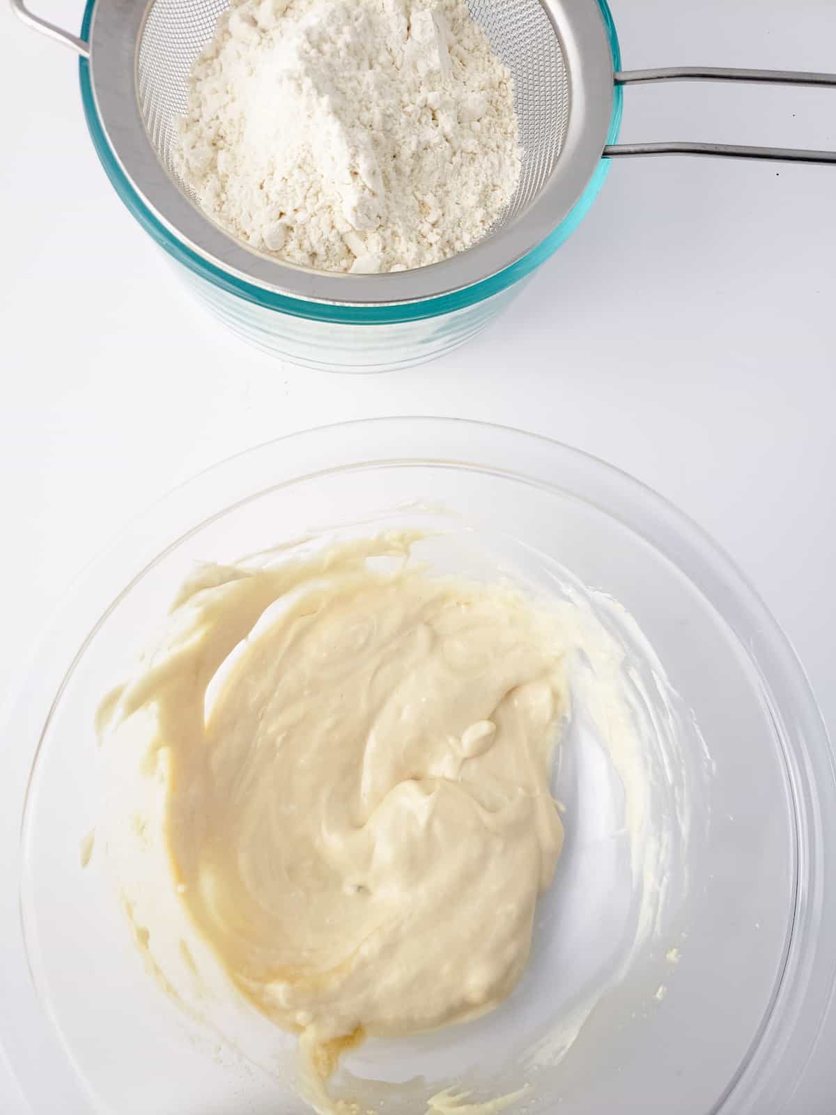 Cream cheese with vanilla and syrup in a bowl with bowl of flour.