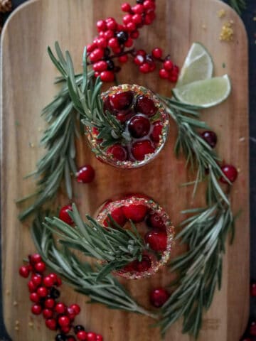 Cranberry mimosas on a wood board with cranberries, rosemary, and lime.
