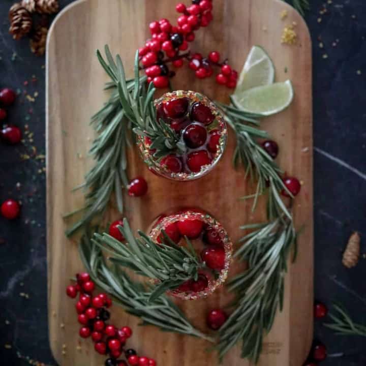Cranberry mimosas on a wood board with cranberries, rosemary, and lime.