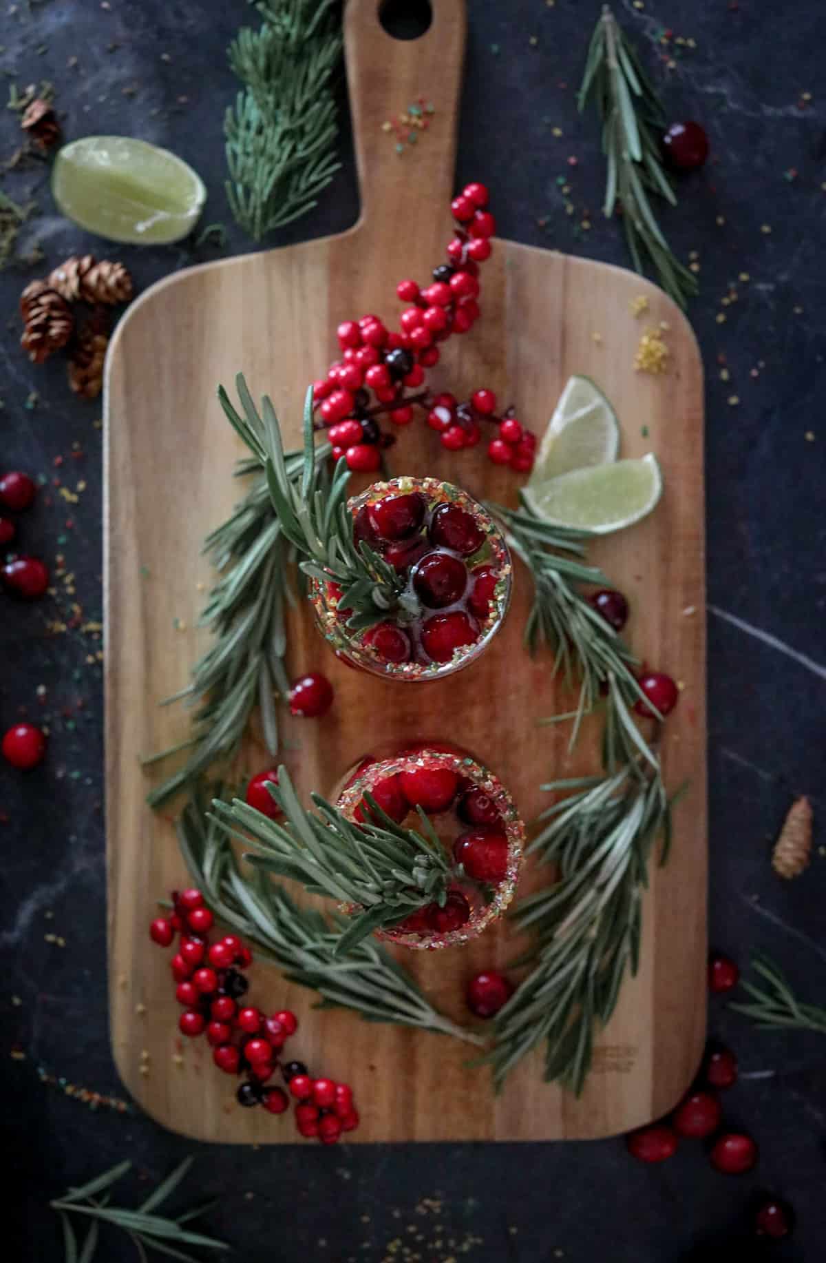 Cranberry Mimosas on a wood cutting board with rosemary, limes, and fresh cranberries.
