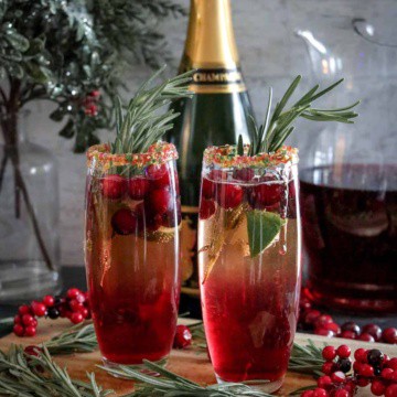 Cranberry mimosas on a wood board with champagne in background.
