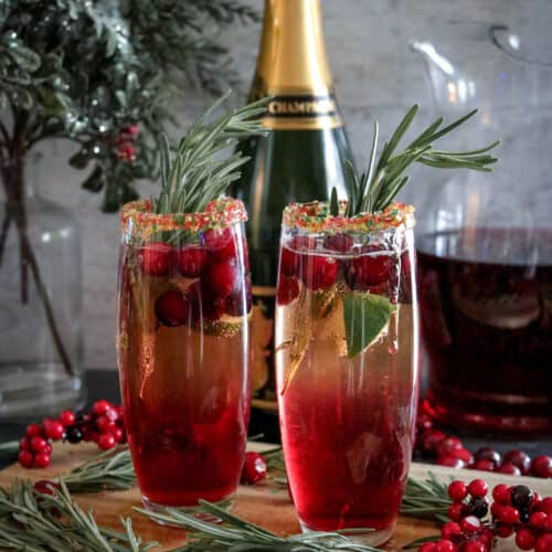 Cranberry mimosas on a wood board with champagne in background.
