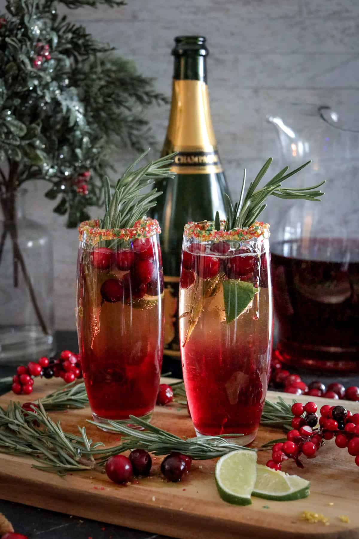 Cranberry mimosa cocktails on a wood cutting board with fresh cranberries, limes, and rosemary.