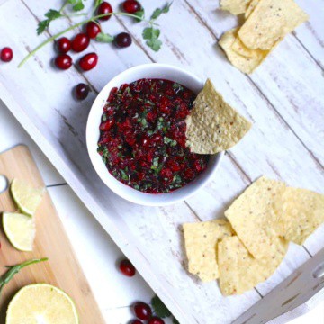 Cranberry Salsa in a white bowl on a white tray with fresh cranberries and cilantro and chips.