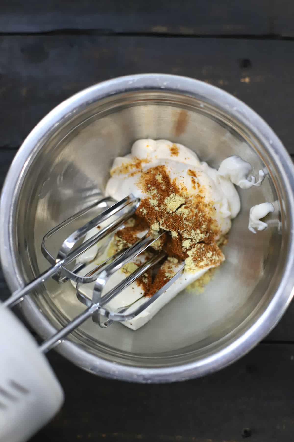Cream cheese, mayo, and spices in a stainless bowl with a mixer.