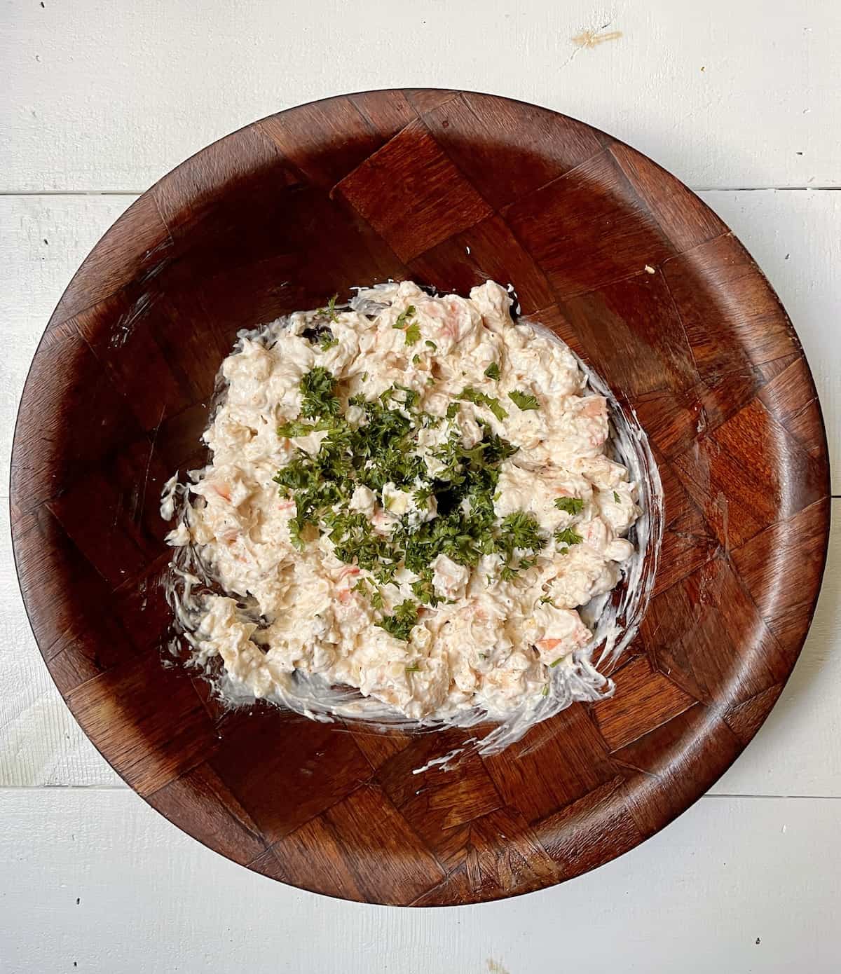 Shrimp dip mixture with parsley in wood bowl on white table.