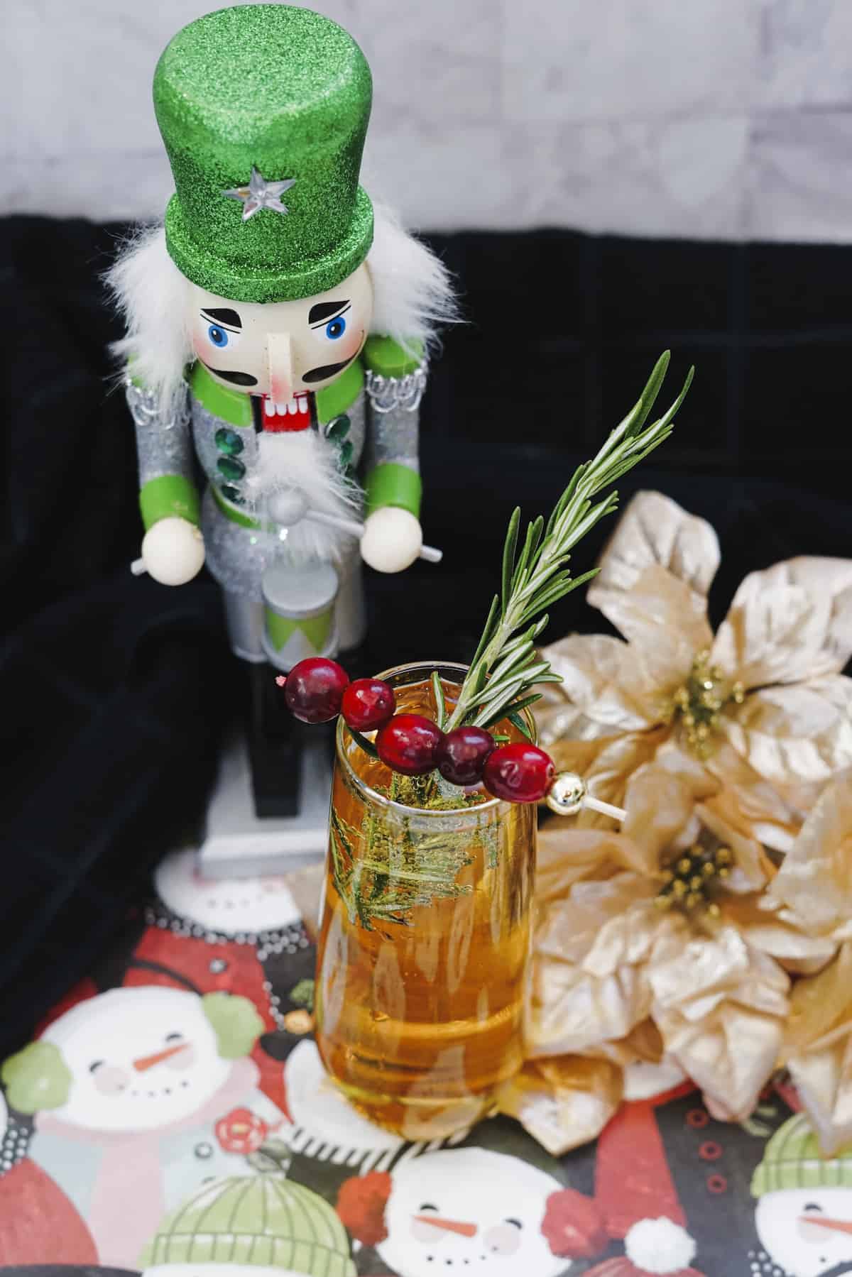 Mimosa cocktail in fluted glass with fresh cranberries and rosemary with green nutcracker and gold flowers in background.