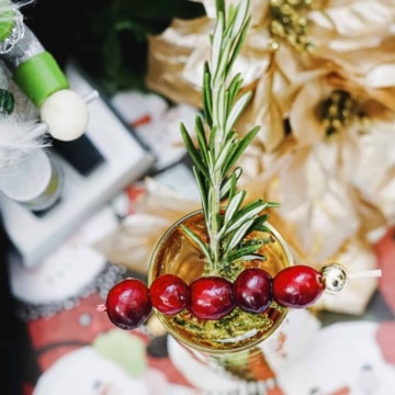 White cranberry juice mimosa with cranberries and rosemary in a fluted glass.
