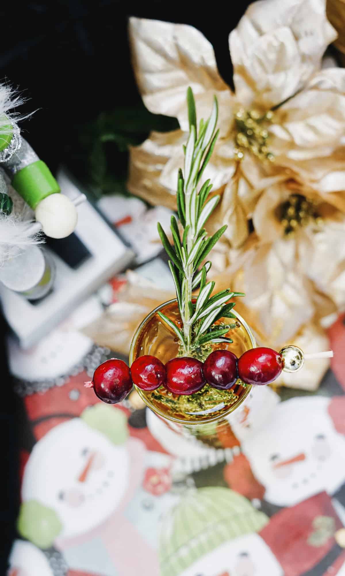 Mimosa cocktail in fluted glass with fresh cranberries with green nutcracker and gold flowers in background.