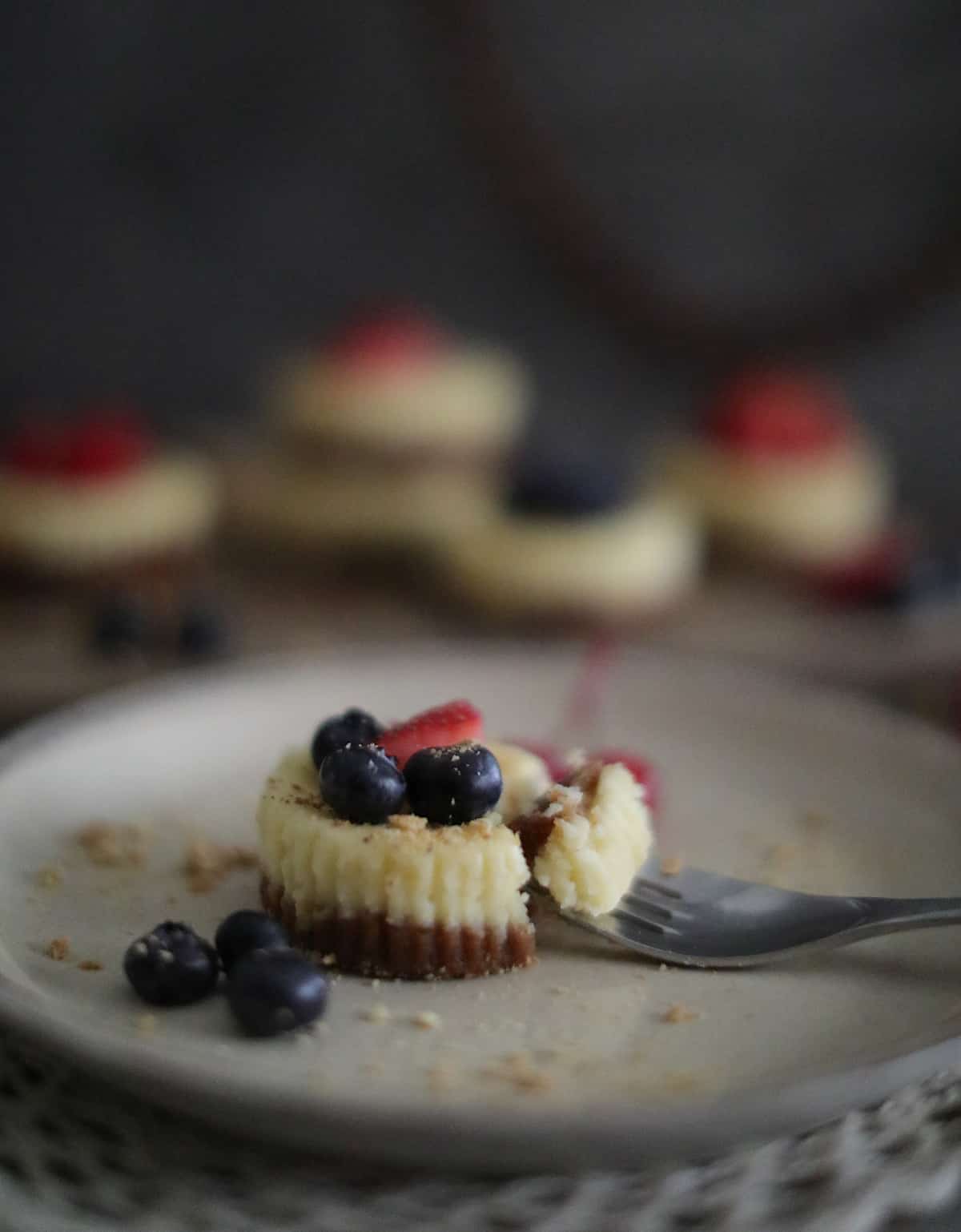 Cheesecake bites with blueberries and strawberry on a white plate.
