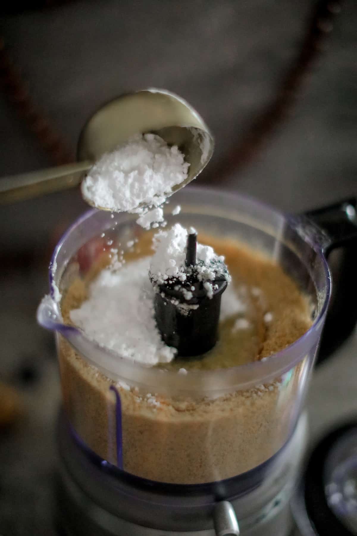 Powdered sugar going into a food processor with graham crackers.