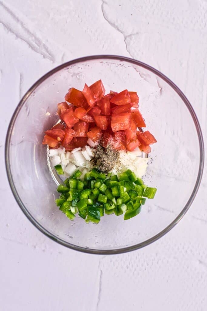Jalapeño, tomato, onion, salt, pepper, lime juice, cilantro in a glass bowl.