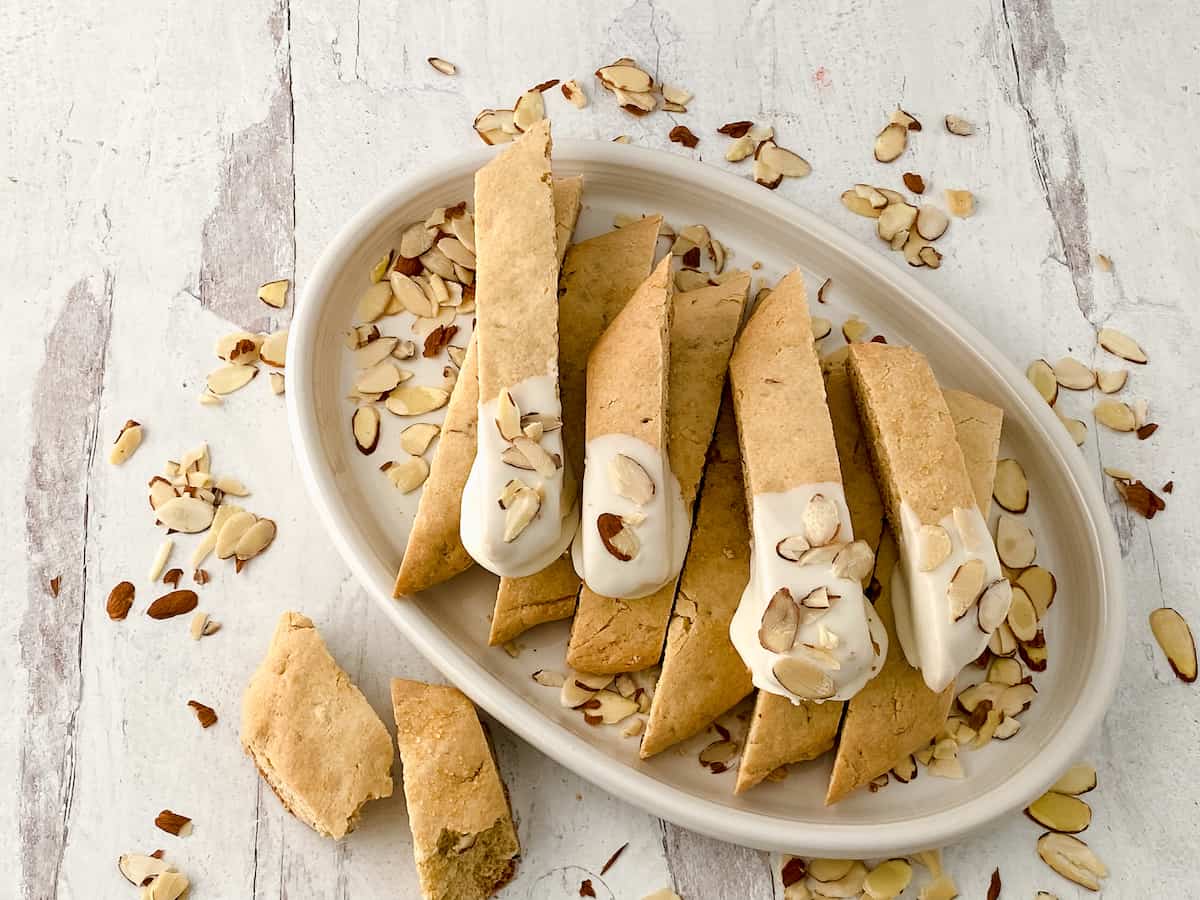 Biscotti dipped in white chocolate and almonds on a white table.