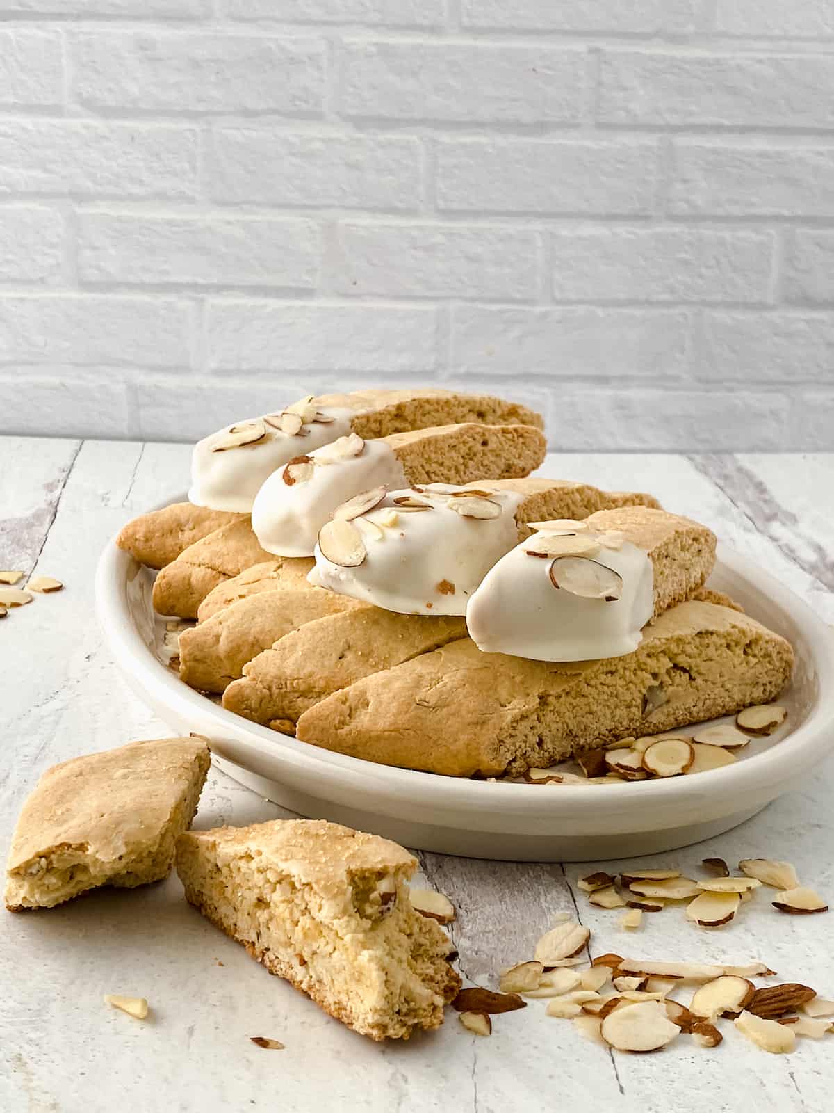 Biscotti dipped in white chocolate and almonds on a white table.