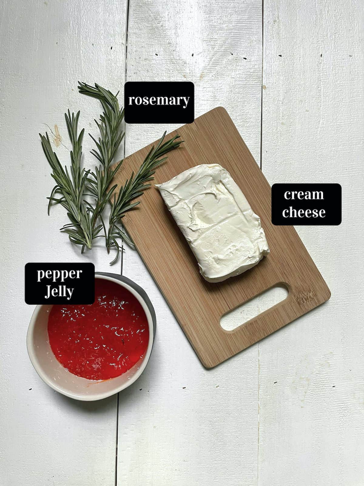 Cream cheese, red pepper jelly, and rosemary on a white board.