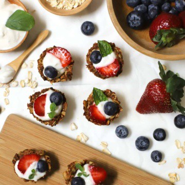 Oatmeal cups filled with yogurt and fruit on a cutting board on a white table with fruit and mint.