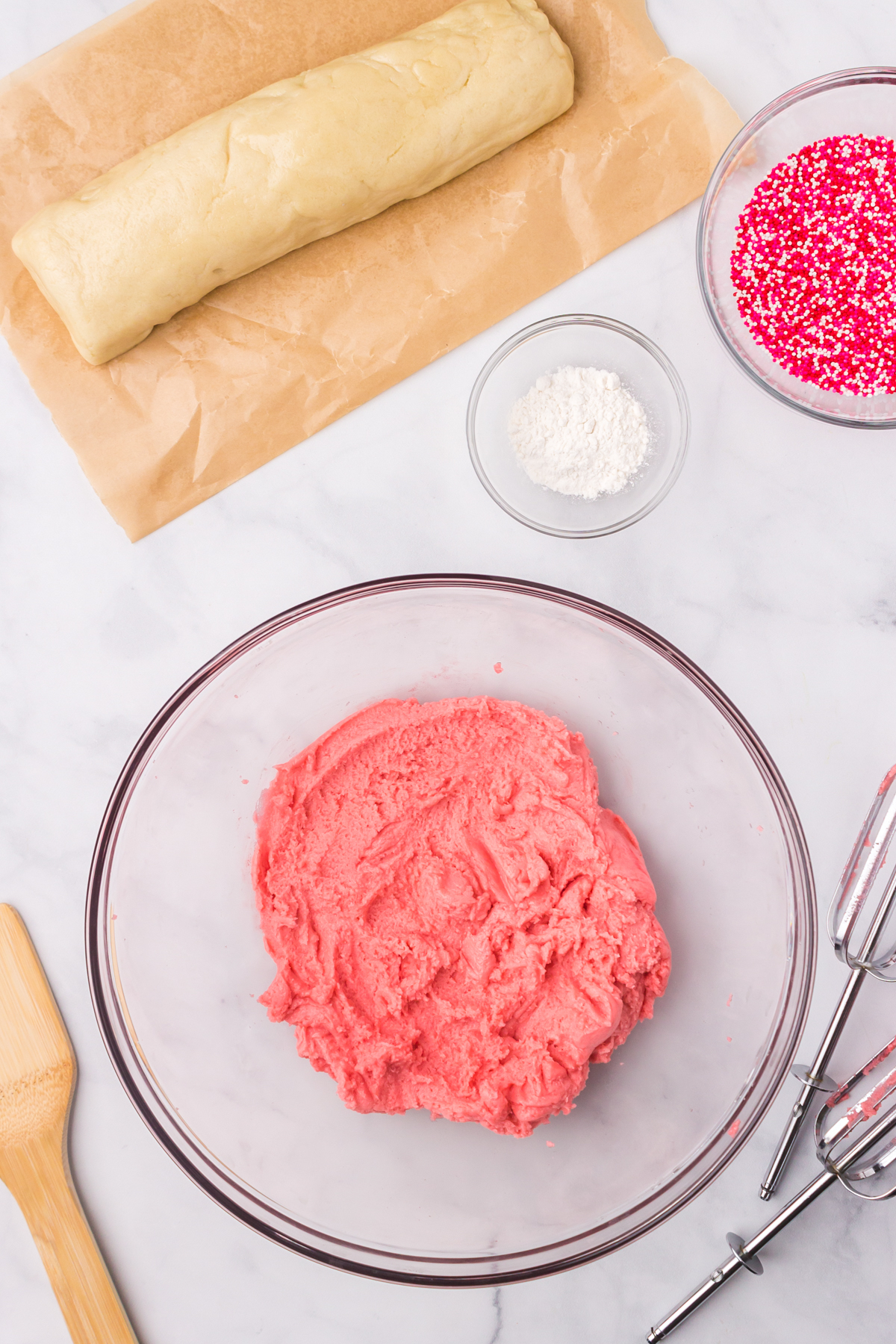 Sugar cookie dough dyed pink with sprinkles, flour, and dough in background.
