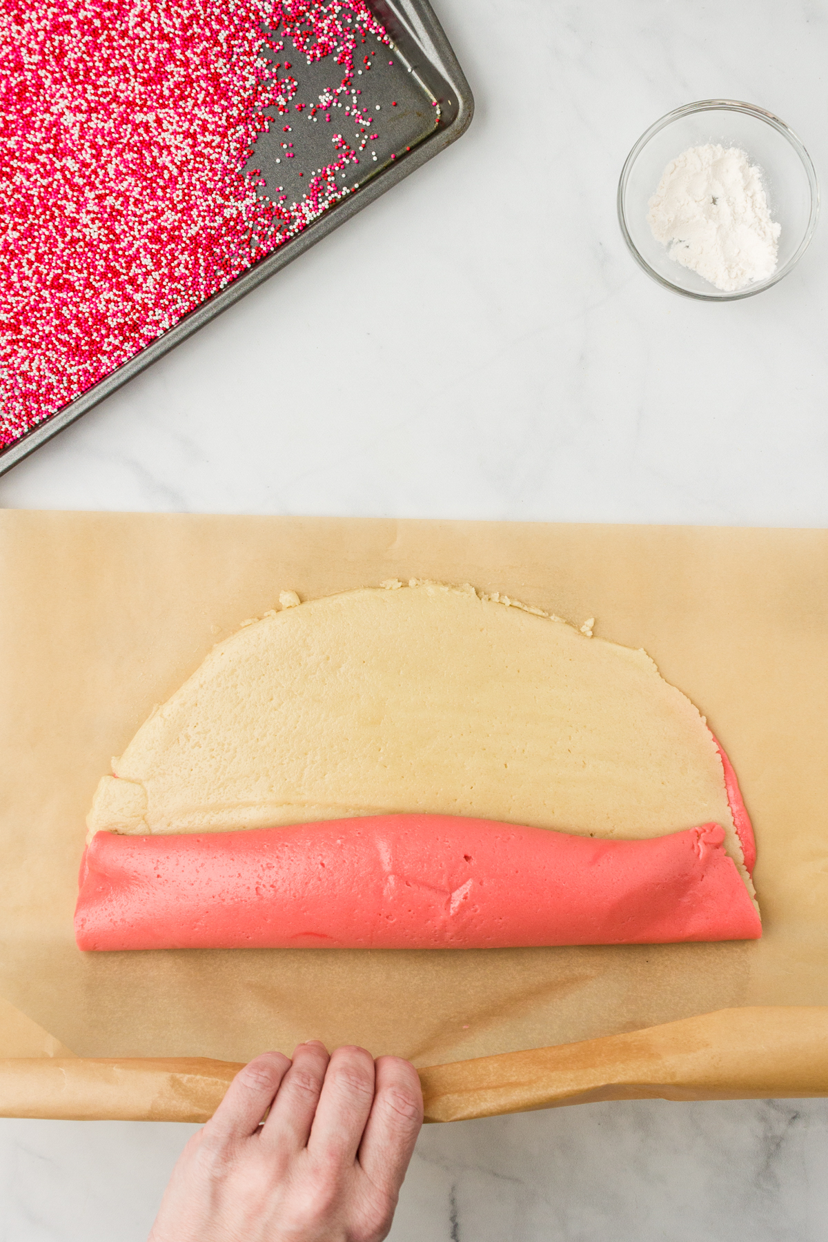 Both red and plain dough rolling into a new combined roll for pinwheel cookie recipe.